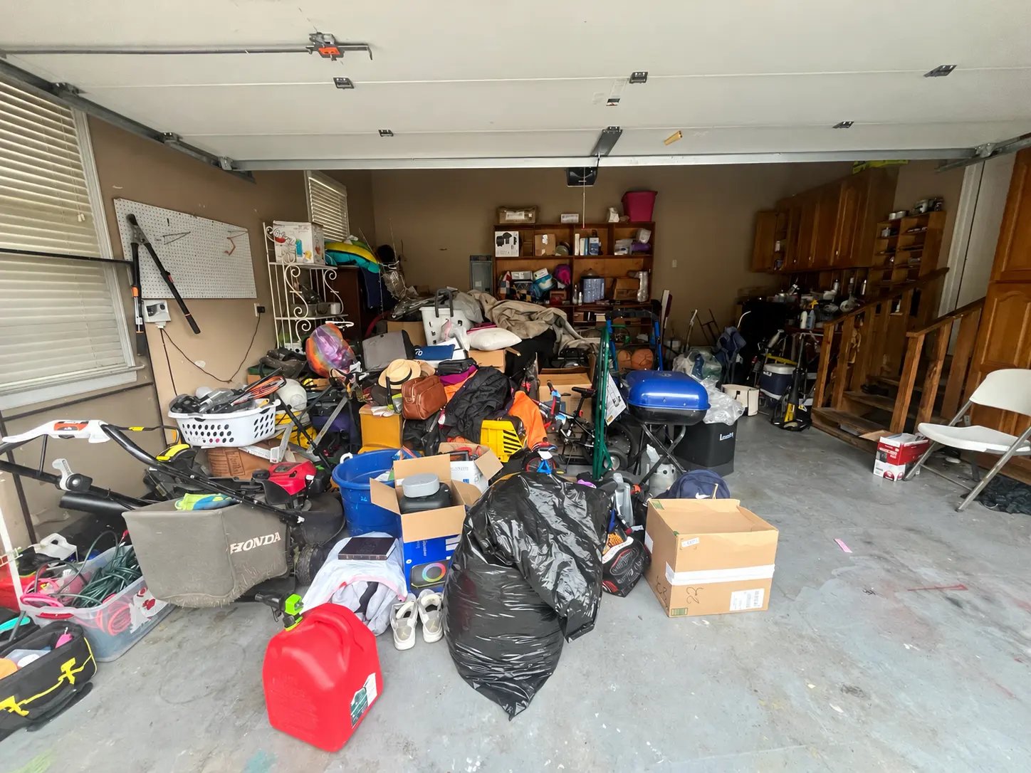Before: two-car garage filled with a lawn mower, bags, boxes, bins, a grill, and household items across the floor